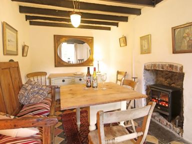 A dining room with a wooden table chairs a bench a fireplace and a mirror at Buck Cottage in Red Wharf Bay