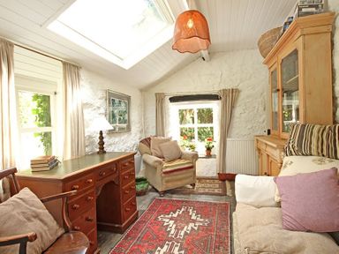 A sitting room with wooden desk armchair sofa and cabinet at Buck Cottage in Red Wharf Bay