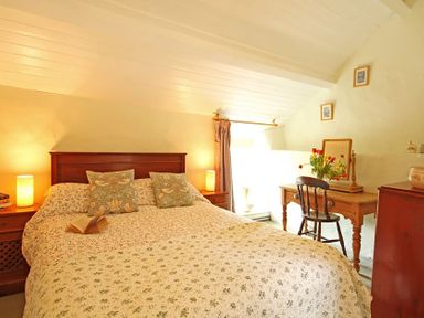 A bedroom with a bed small bedside tables lamps a wooden dressing table with a mirror flowers and a chair at Buck Cottage in Red Wharf Bay