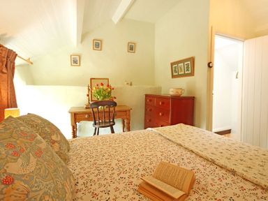 A bedroom with a bed a wooden desk with flowers a chair and a chest of drawers at Buck Cottage in Red Wharf Bay