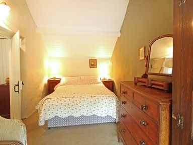 A bedroom with a bed between two bedside tables and a wooden dresser with a mirror at Buck Cottage in Red Wharf Bay