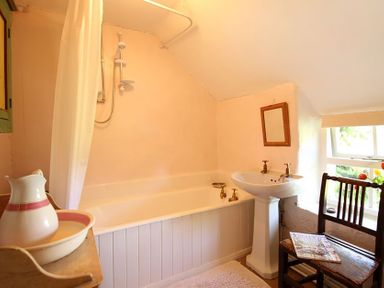 A bathroom with a bathtub sink chair and a window at Buck Cottage in Red Wharf Bay