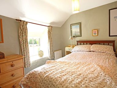 A bedroom with a bed covered in floral bedding a wooden dresser and floral curtains at Buck Cottage in Red Wharf Bay