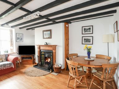 A living room with a wooden fireplace a round dining table with chairs and a television at Cae Person in Llangoed