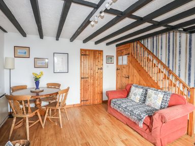 A living room with a wooden dining table and chairs a red sofa under wooden stairs and wooden doors at Cae Person in Llangoed