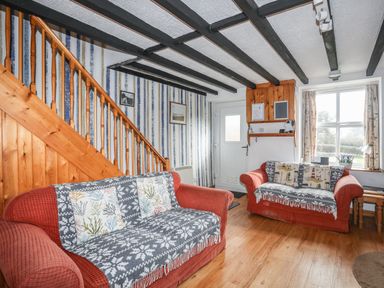 A sitting room with two red sofas wooden stairs and a front door at Cae Person in Llangoed