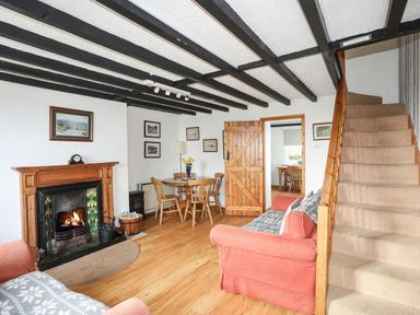 A living room with a fireplace wooden dining table chairs and carpeted stairs at Cae Person in Llangoed