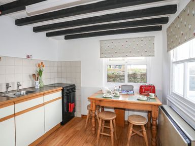 A kitchen with wooden table stools cooker and window blinds with duck pattern at Cae Person in Llangoed