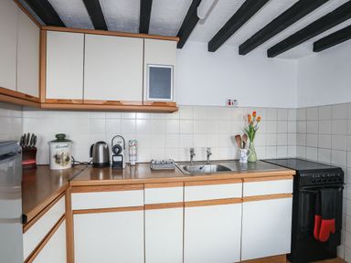A kitchen with white cabinets a sink a kettle a coffee machine utensils and a stove at Cae Person in Llangoed