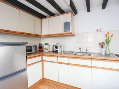 A kitchen with cabinets a refrigerator a microwave kettle a sink and flowers in a vase at Cae Person in Llangoed
