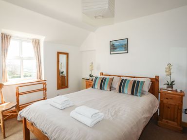 A bedroom with a wooden bed with two striped pillows and folded towels on the bed two wooden bedside tables with plants a chair and a window in the room at Cae Person in Llangoed