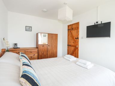 A bedroom with a bed, wooden wardrobe, wooden chest of drawers, a wall-mounted TV, and a wooden door at Cae Person in Llangoed