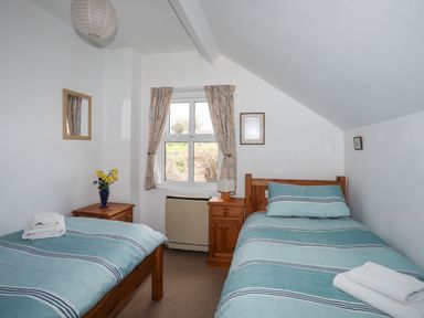 A bedroom with two single beds a window with curtains and wooden nightstands at Cae Person in Llangoed