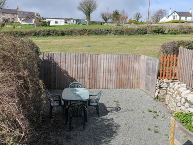 A small fenced outdoor patio area with a plastic table and four chairs at Cae Person in Llangoed