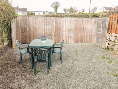 An outdoor area with a plastic table and four chairs on gravel near a wooden fence at Cae Person in Llangoed