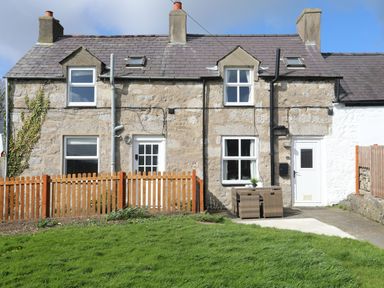 The back of a stone house with windows doors a wooden fence a small patio set and a grassy lawn at Cae Person in Llangoed