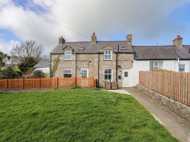 A stone and white-painted terraced house with a green lawn and wooden fences at Cae Person in Llangoed