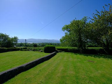 A grassy garden with a stone wall a hedge and trees under a clear blue sky at Cae Person in Llangoed