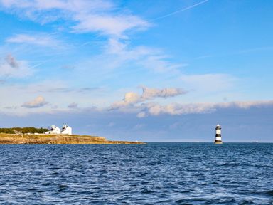 A coastline with white buildings on the left and a striped lighthouse in the water at Cae Person in Llangoed