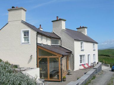 A white two-story house with multiple chimneys and a glass extension on a gravel driveway in a rural area at Cae'r Dyni Criccieth