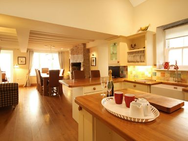 A kitchen with wooden countertops a dining table with chairs and a stone fireplace at Cae'r Dyni (Caer Dyni) in Criccieth