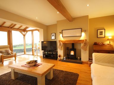A living room with a wood burning stove television armchairs and a wooden table at Cae'r Dyni (Caer Dyni) in Criccieth