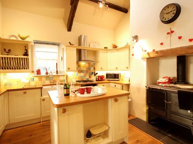 A kitchen with a central island wooden countertops a stove microwave and a wall clock at Cae'r Dyni Criccieth