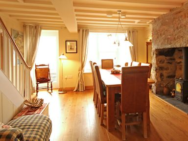 A dining room with a wooden table and chairs near a stone fireplace at Cae'r Dyni (Caer Dyni) in Criccieth