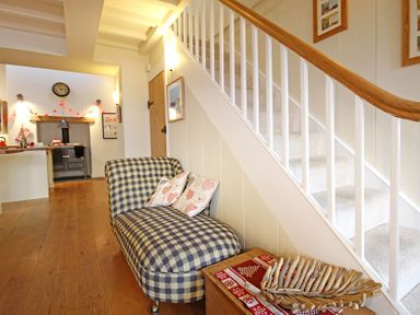 A hallway with a checked upholstered bench under stairs and a kitchen visible in the background at Cae'r Dyni (Caer Dyni) in Criccieth