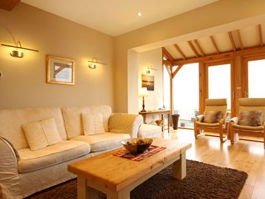 A living room with a sofa two chairs a wooden table and a lamp at Cae'r Dyni (Caer Dyni) in Criccieth