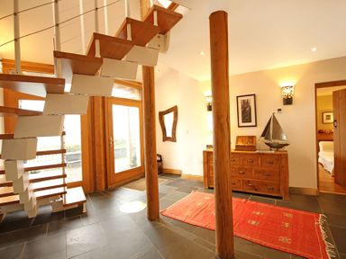 An entryway with wooden stairs two wooden poles a wooden dresser with a model sailboat and a red rug on the floor at Cae'r Dyni (Caer Dyni) in Criccieth