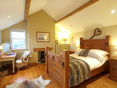 A bedroom with wooden bed frame desk chair chest of drawers and a window at Cae'r Dyni in Criccieth