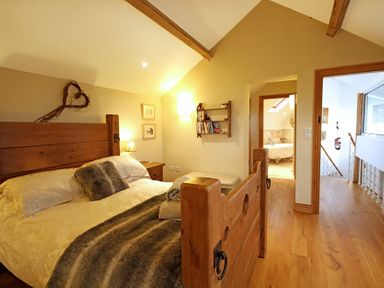 A bedroom with a wooden bed frame a bedside table with lamp a wall shelf and a bathroom visible through an open door at Cae'r Dyni (Caer Dyni) in Criccieth