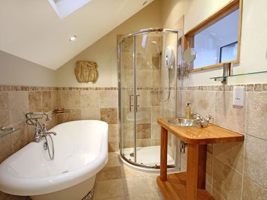 A bathroom with a freestanding bathtub, a glass shower enclosure, and a wooden vanity with a round sink at Cae'r Dyni (Caer Dyni) in Criccieth