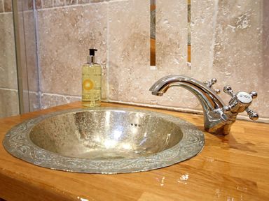 A bathroom sink with a metallic basin a chrome faucet and a soap dispenser on a wooden countertop at Cae'r Dyni Criccieth