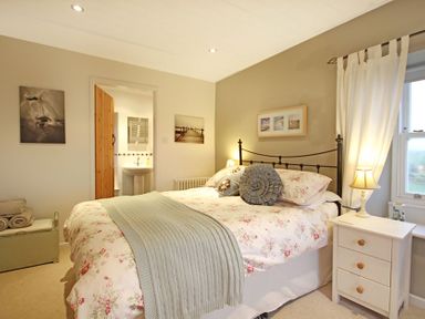 A bedroom with a floral bedspread and pillows a bedside table with a lamp and an open door leading to a bathroom at Cae'r Dyni (Caer Dyni) in Criccieth