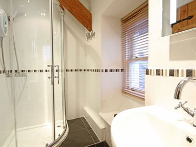 A bathroom with a curved glass shower enclosure a white sink and a window with blinds at Cae'r Dyni (Caer Dyni) in Criccieth
