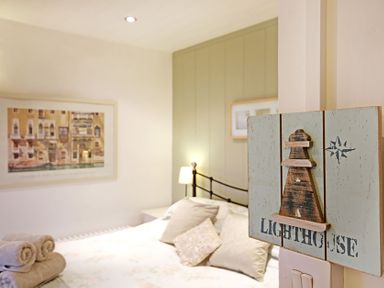 A bedroom with a bed and pillows a lamp towels on the bed a framed picture on the wall and a wooden lighthouse sign at Cae'r Dyni Criccieth