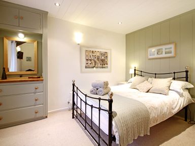 A bedroom with a metal bed frame with folded towels on the bed and a cabinet with a mirror at Cae'r Dyni (Caer Dyni) in Criccieth