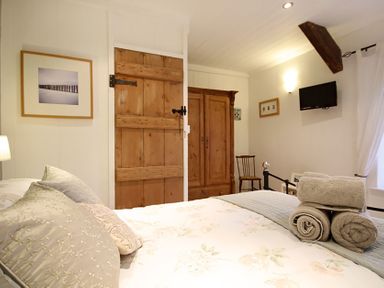 A bedroom with a floral bedspread a wooden door wooden wardrobe and towels on the bed at Cae'r Dyni Criccieth