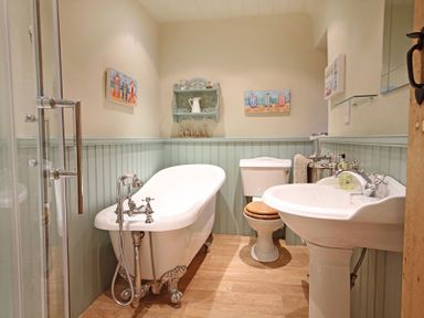 A bathroom with a clawfoot tub toilet sink and shower with green wainscoting and wooden floor at Cae'r Dyni Criccieth