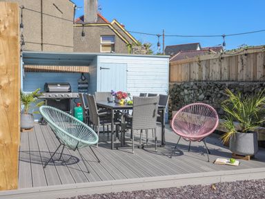 An outdoor patio with a dining table and chairs two round chairs potted plants and a barbecue grill at Cambrian House in Criccieth