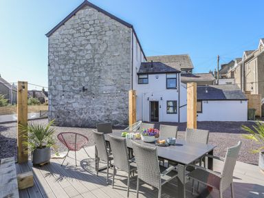 An outdoor patio area with dining table and chairs next to a stone and white building at Cambrian House in Criccieth