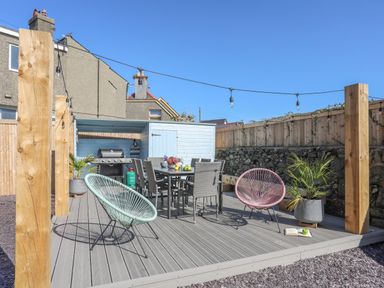 An outdoor patio area with a dining table and chairs two round chairs string lights and potted plants at Cambrian House in Criccieth