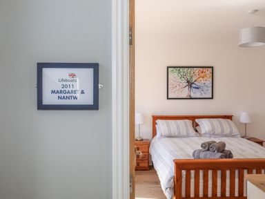 A bedroom with a wooden bed frame two bedside tables with lamps and a tree painting on the wall at Cambrian House in Criccieth