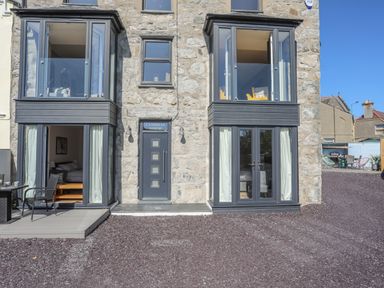 Stone building exterior with two bay windows a central door labeled Cambrian House and outdoor seating at Cambrian House in Criccieth