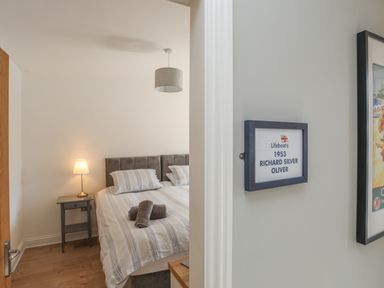 A bedroom with a double bed with striped bedding a bedside table with a lamp and rolled towels on the bed at Cambrian House in Criccieth