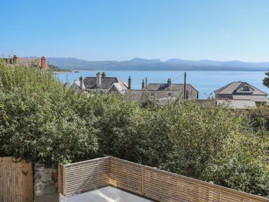 A view of rooftops and greenery with mountains and a body of water in the background at Cambrian House in Criccieth