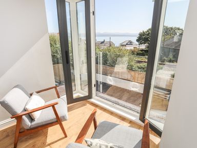 A seating area with two armchairs beside large glass doors overlooking a garden and distant sea view at Cambrian House in Criccieth
