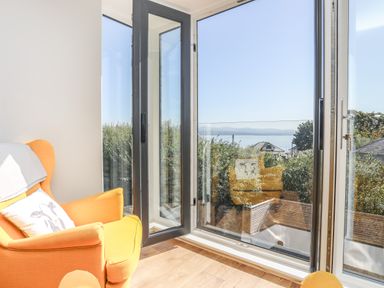 An orange armchair next to open glass doors overlooking a garden and water at Cambrian House in Criccieth